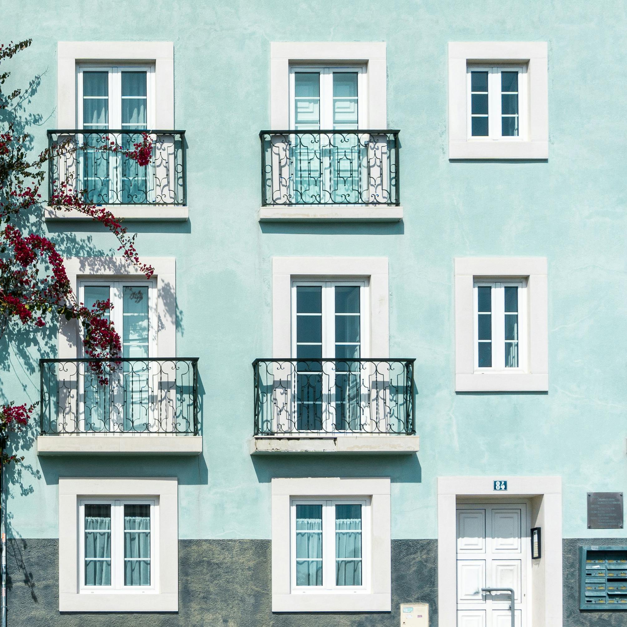 Exterior view of a pastel-colored building in Lisbon, featuring ornate iron balconies and bright windows.